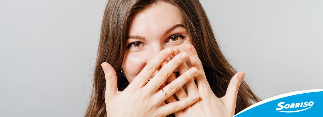 Mulher sorrindo e tampando a boca depois de se livrar do mau hálito