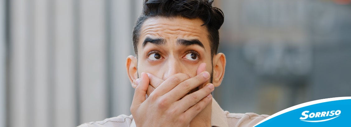 Homem tapando a boca por causa do bafo