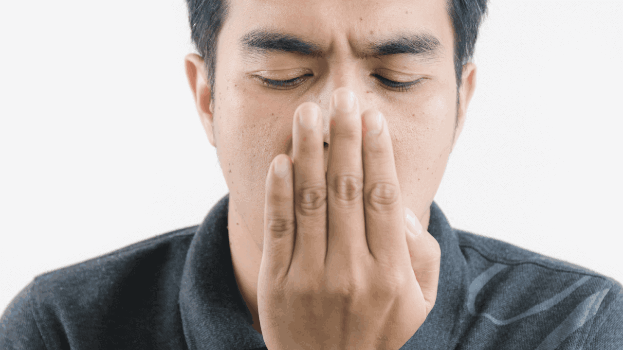 Homem com a mão em frente a boca, checando o hálito para descobrir se precisa de uma bala de hortelã